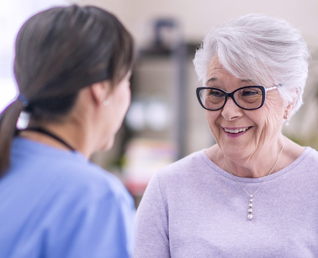 Healthcare worker speaking with smiling elderly woman, featured in Viatris public policy section on community health.